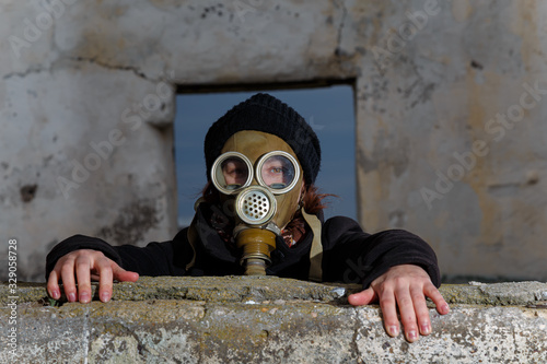 Human in gas mask looking for a way out through window inside ruined building. Enviromental pollution, ecology disaster, radiation, biological hazard concept. Frame in frame composition.