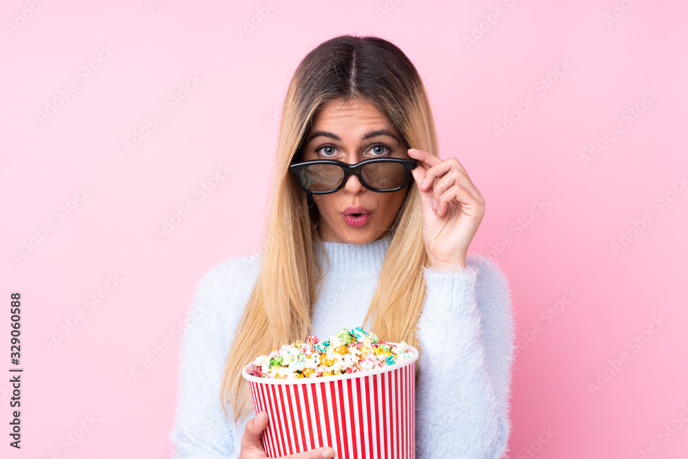 Young Uruguayan woman over isolated pink background surprised with 3d glasses and holding a big bucket of popcorns Young Uruguayan woman over isolated pink background surprised with 3d glasses and holding a big bucket of popcorns
