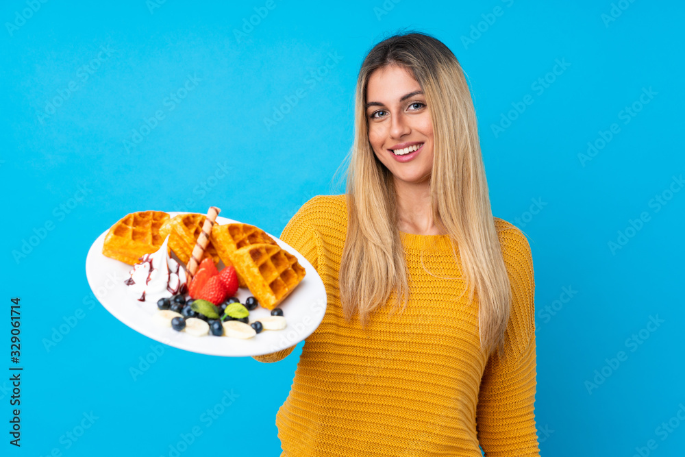 Young woman holding waffles over isolated background with happy expression Young woman holding waffles over isolated background with happy expression