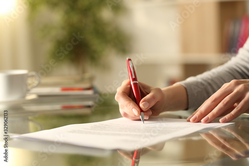 Woman signing document with pen on a desk at home photo