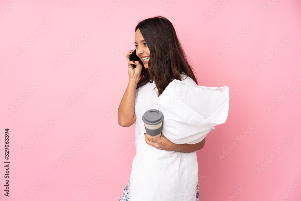 Young woman in pajamas isolated on pink background holding coffee to take away and a mobile Young woman in pajamas isolated on pink background holding coffee to take away and a mobile