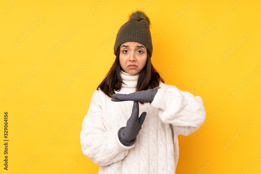 Young woman with winter hat over isolated yellow background making time out gesture Young woman with winter hat over isolated yellow background making time out gesture