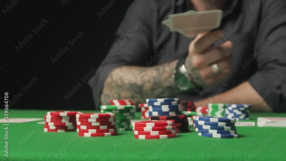 A man with tattoo winning game, grabbing all chips sitting at poker table