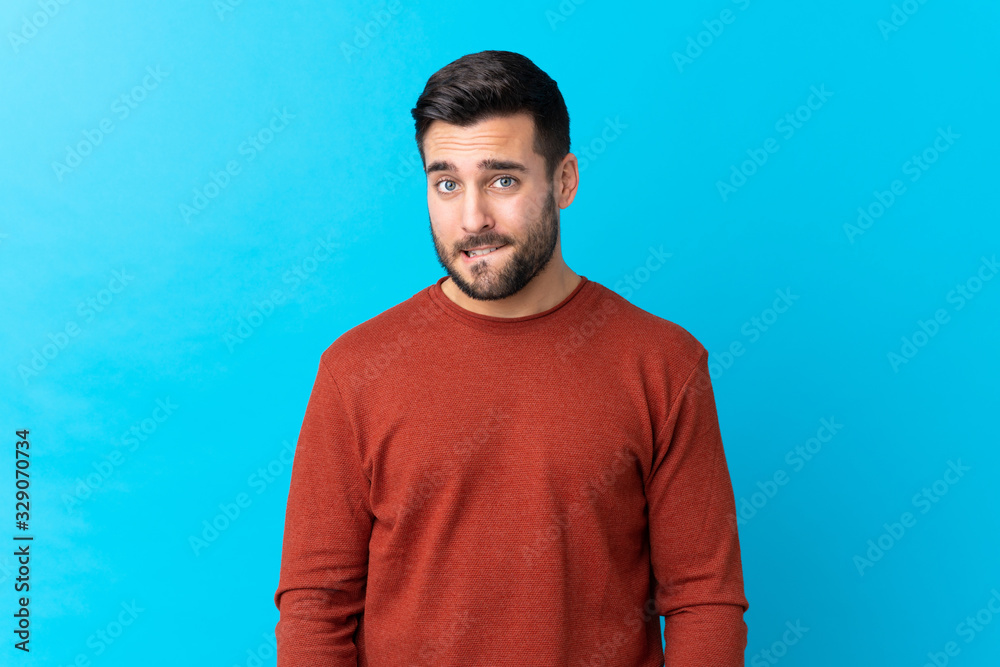 Young handsome man with beard over isolated blue background having doubts and with confuse face expression Young handsome man with beard over isolated blue background having doubts and with confuse face expression