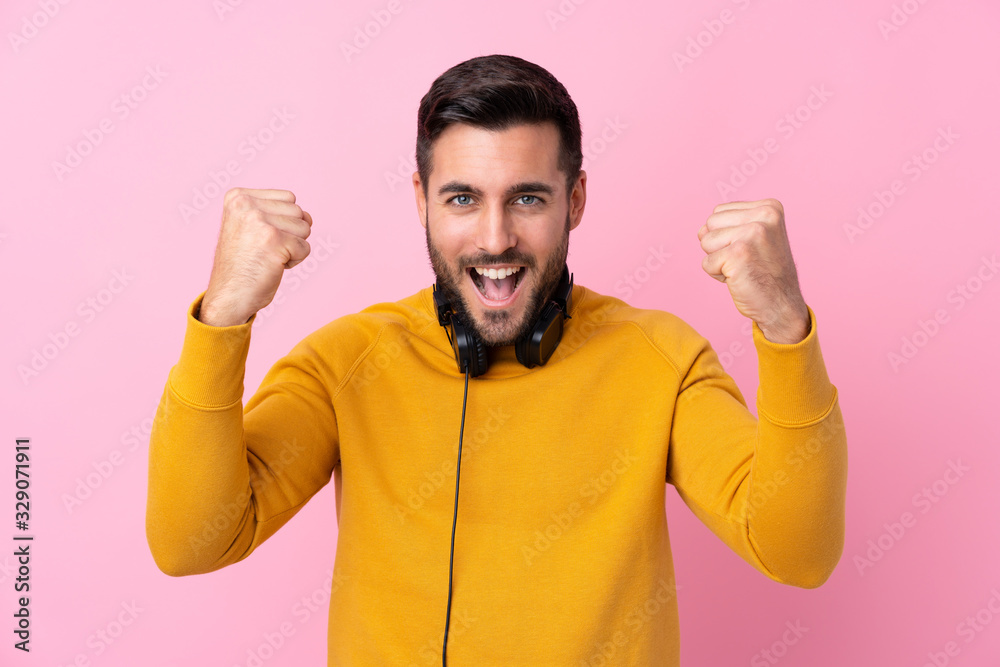 Young handsome man with earphones over isolated pink background celebrating a victory Young handsome man with earphones over isolated pink background celebrating a victory