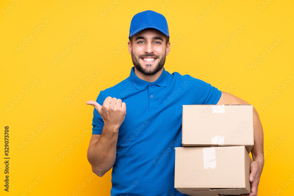 Delivery man over isolated yellow background pointing to the side to present a product Delivery man over isolated yellow background pointing to the side to present a product