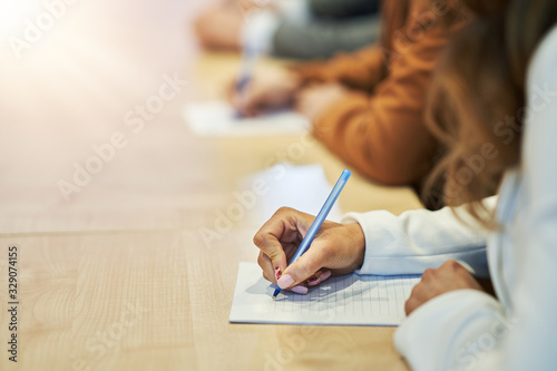 Picture of a human hand writing something on the paper on the foreground