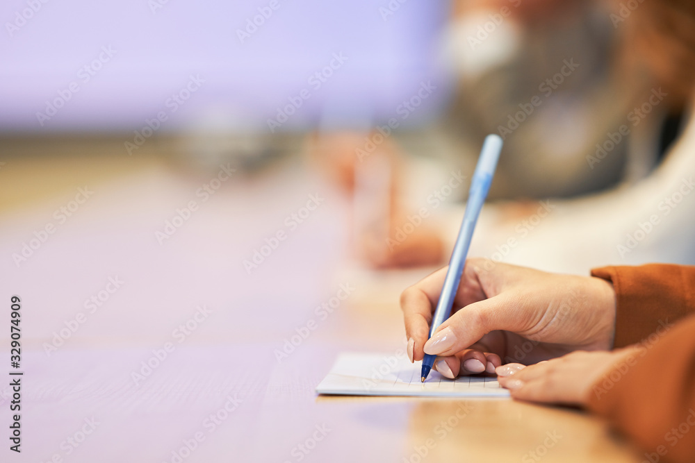 Picture of a human hand writing something on the paper on the foreground Picture of a human hand writing something on the paper on the foreground