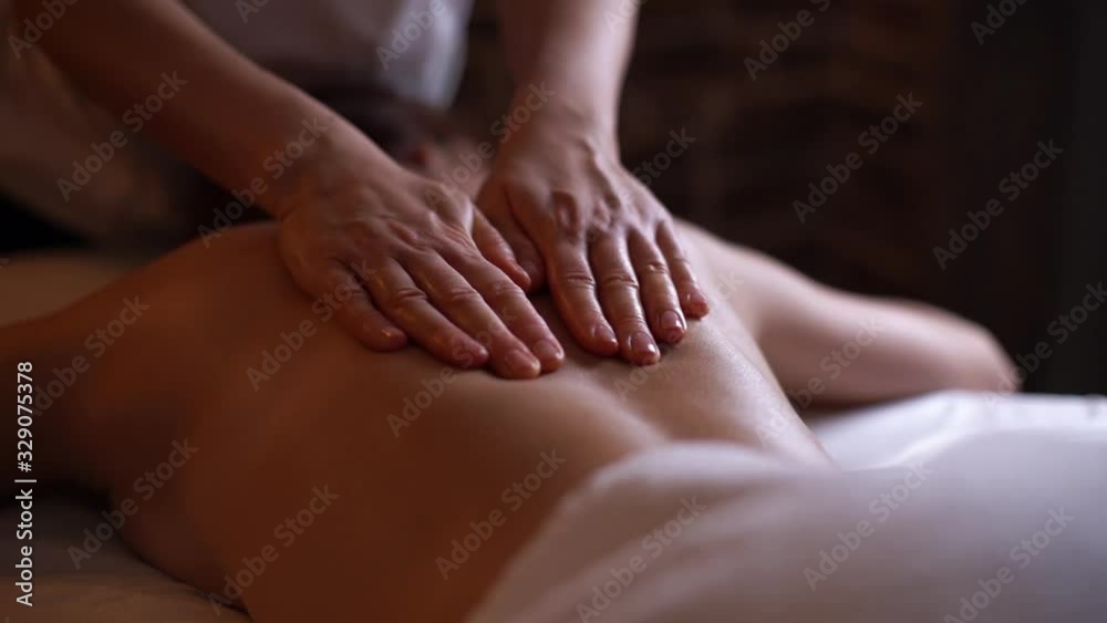 Young unrecognizable woman gets professional back massage in spa salon. Beautiful naked girl with perfect skin gets relaxing massage. Concept of luxury professional massage. Shooting in slow motion.