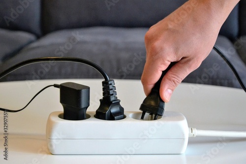 Male hand connecting an electrical plug to a power strip. Multi-socket power strip. Concept of electricity savings, increases, costs