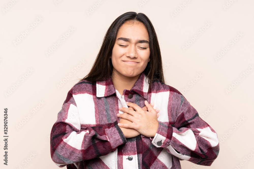 Young Indian woman isolated on beige background having a pain in the heart Young Indian woman isolated on beige background having a pain in the heart