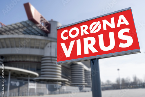 Red warning sign for Covid-19 in front of closed stadium. Concept of cancellation of sporting events due to corona virus medical emergency. Purposely blurred stadium in the background.