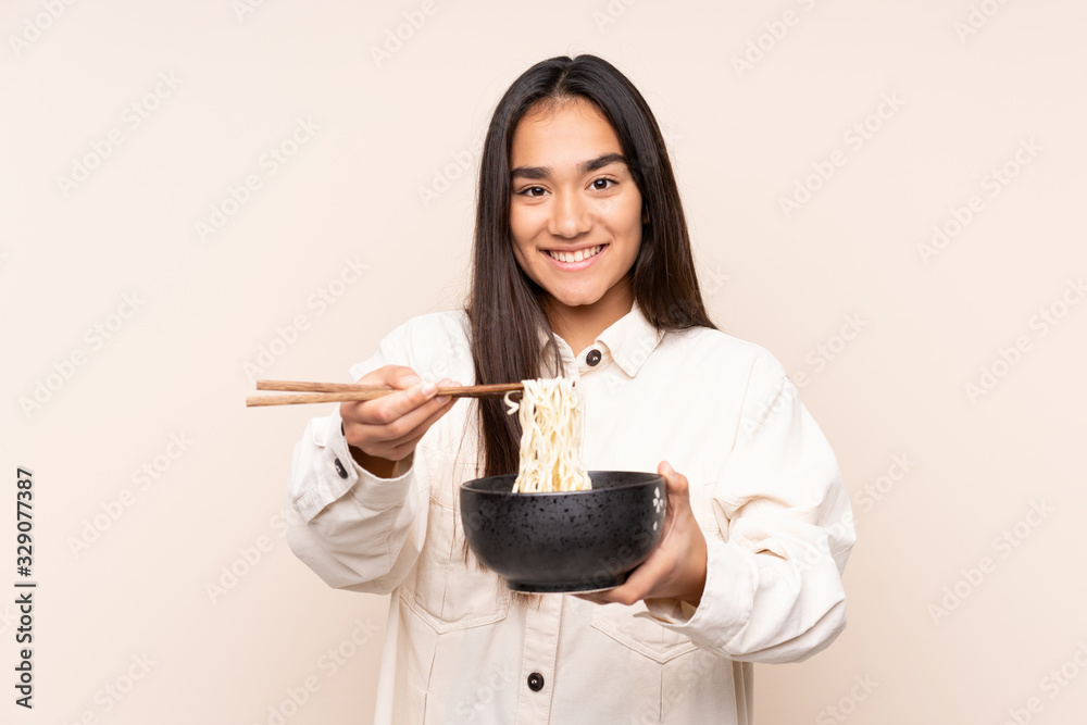 Young Indian woman isolated on beige background holding a bowl of noodles with chopsticks and offering it Young Indian woman isolated on beige background holding a bowl of noodles with chopsticks and offering it
