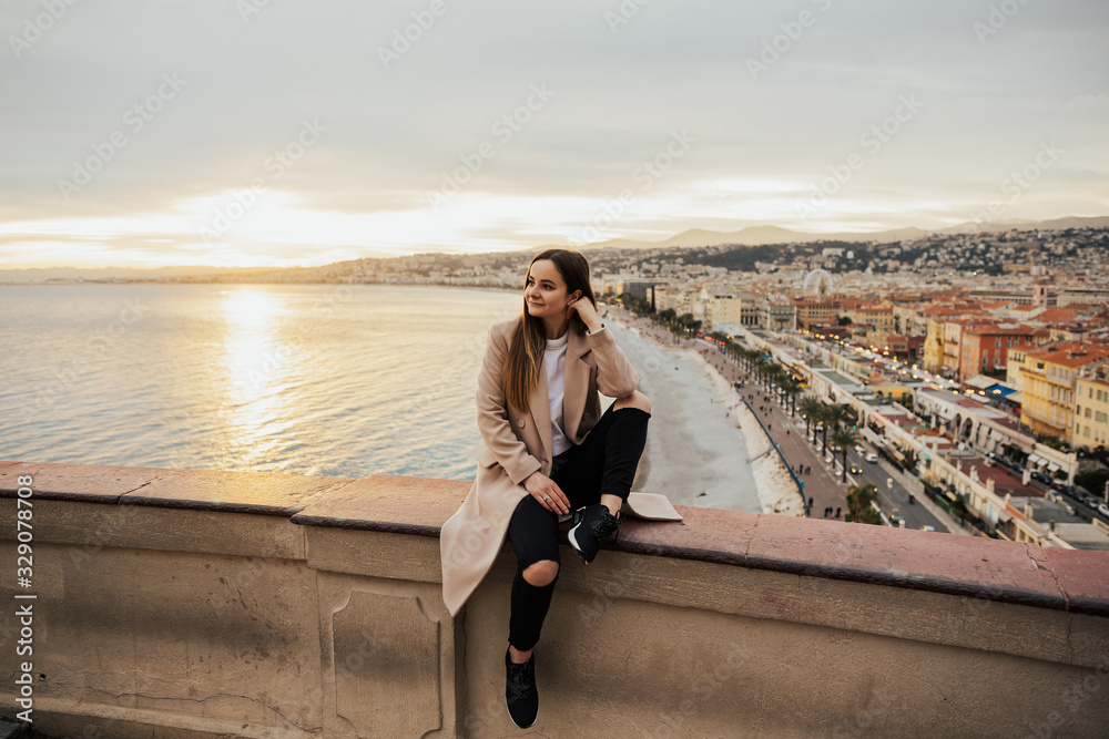 Young traveler girl in a nice outfit enjoying her holidays on a Mediterranean coast while sunset sky and see is beautiful. Lifestyle concept. Youth and happiness. Young traveler girl in a nice outfit enjoying her holidays on a Mediterranean coast while sunset sky and see is beautiful. Lifestyle concept. Youth and happiness.