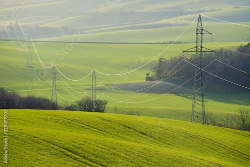 Power lines pylons with stretched cables in undulating spring field, no sky Fototapet