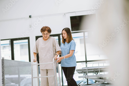 young physical therapist helping senior patient in using walker during rehabilitation