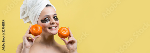 Beauty portrait of woman in white towel on head with gold nourishing mask on face. Skincare cleansing eco organic cosmetic spa relax concept. A girl stands with her back holding an orange mandarin. © Mountains Hunter