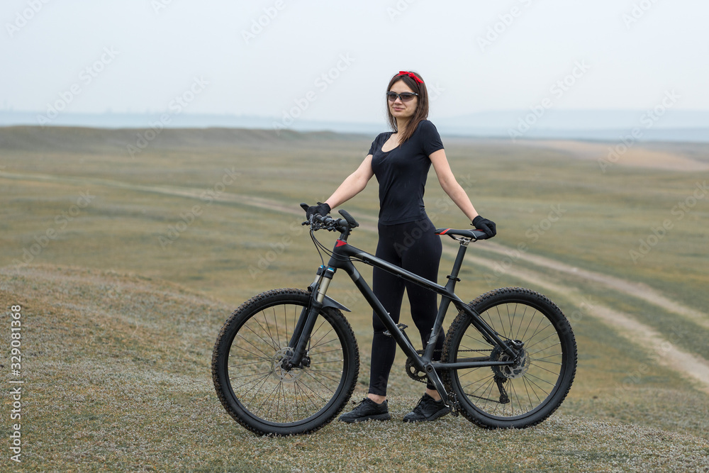 Girl on a mountain bike on offroad, beautiful portrait of a cyclist in rainy weather, Fitness girl rides a modern carbon fiber mountain bike in sportswear. Close-up portrait of a girl in red bandana.