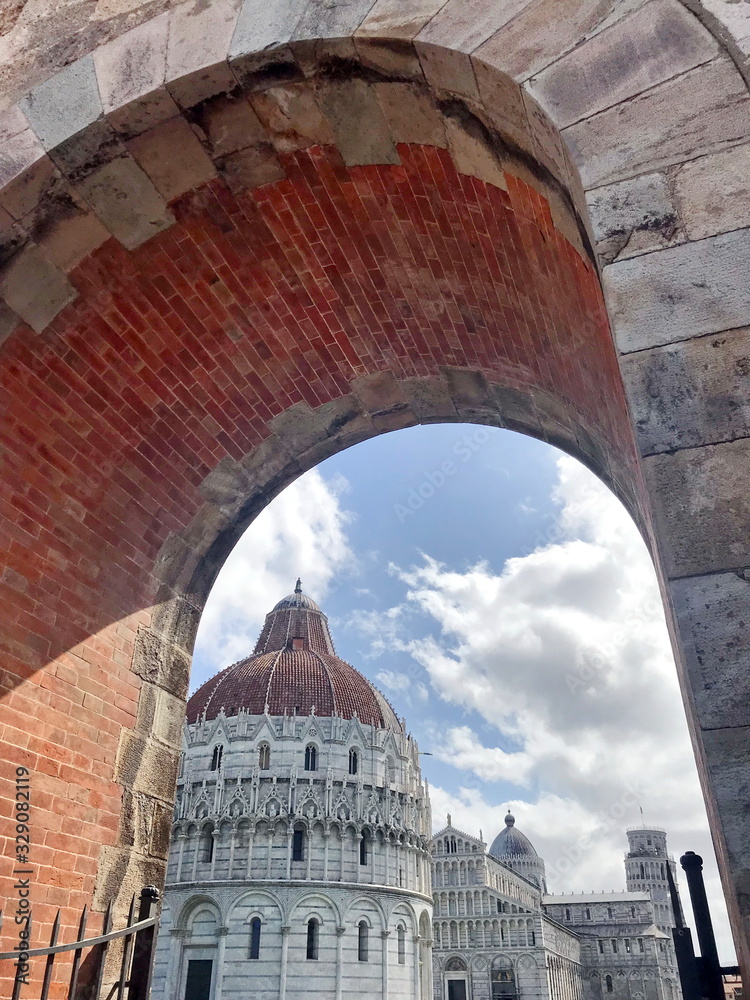 View from the gates of a medieval fortress on the famous Leaning Tower of Pisa on a cloudy blue sky.
