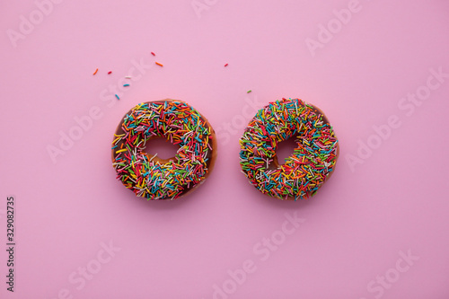 Two classic chocolate donuts with colorful sprinkles on pink background. Sweet dessert for holiday party. 