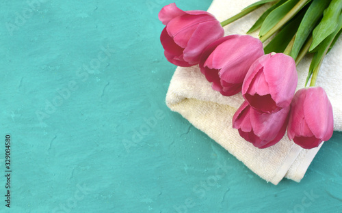 Spa composition with pink tulips and towel on turquoise background. Concept for wedding, relax or organic cosmetics. Copyspace. Banner.
