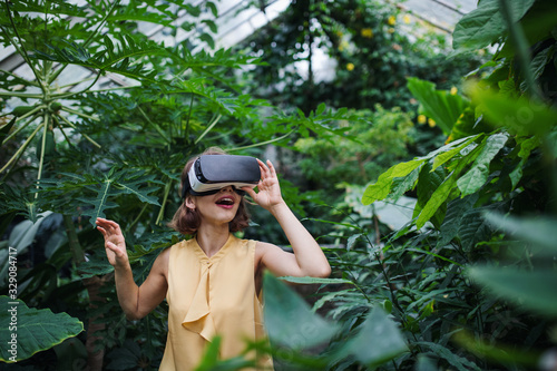 Front view of young woman standing in botanical garden, using VR glasses.
