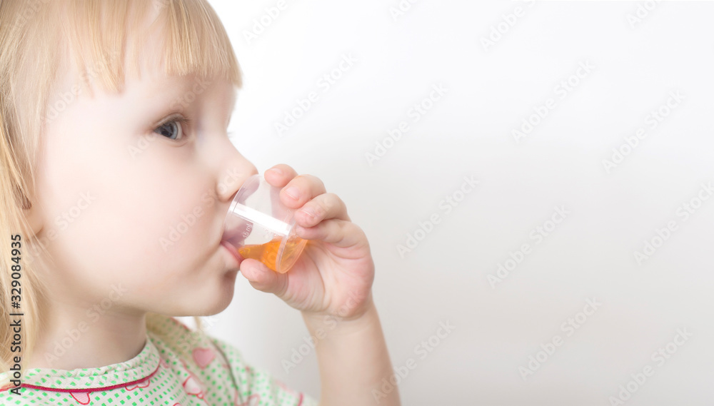 Little girl drinks cough syrup in a measuring cup for children. The