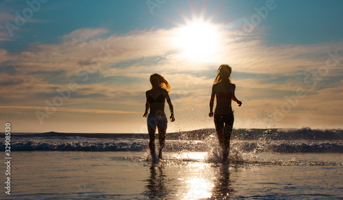 Wallpaper Mural Silhouette of two beautiful women running on a beach shore with waves in the background at sunset or sunrise. Torontodigital.ca