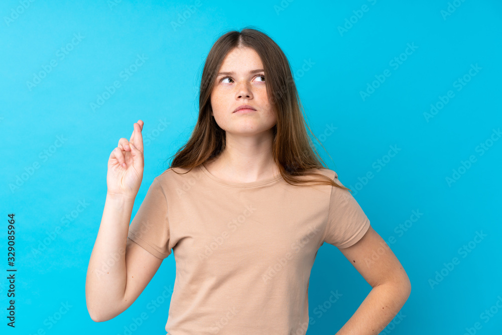 Fototapeta premium Ukrainian teenager girl over isolated blue background with fingers crossing and wishing the best