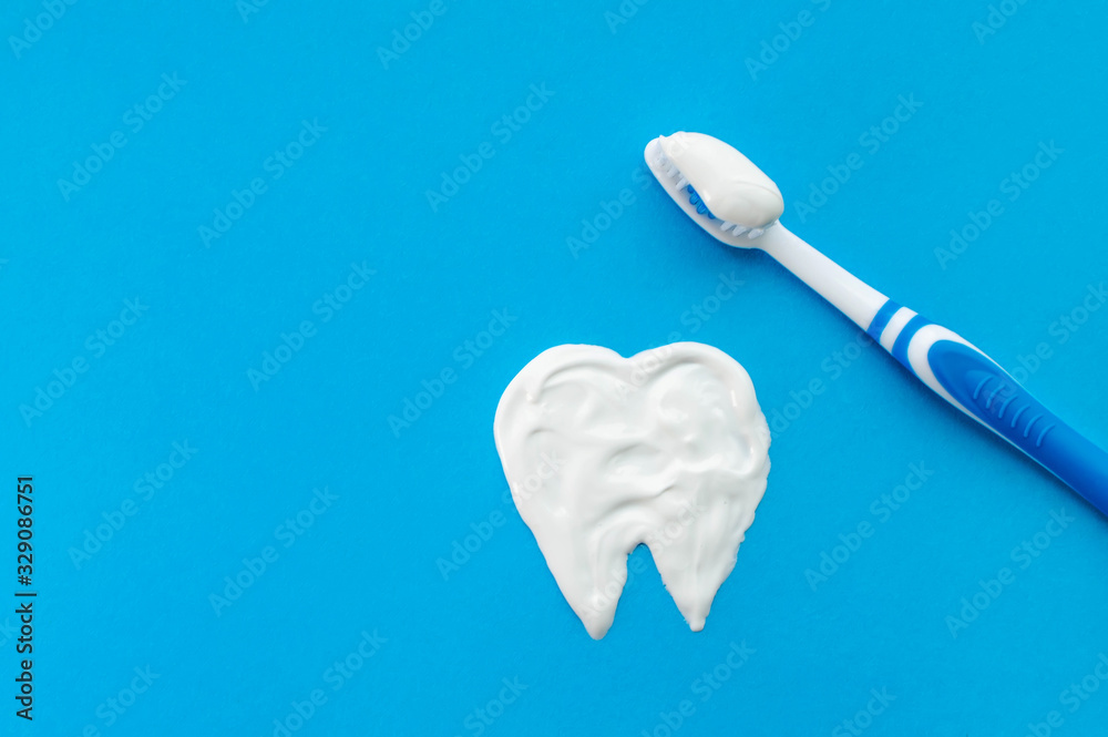 Blue toothbrush on a blue background with a tooth pattern drawn with toothpaste. The view from the top. Blue toothbrush on a blue background with a tooth pattern drawn with toothpaste. The view from the top.