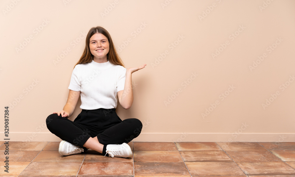 Ukrainian teenager girl sitting on the floor holding copyspace imaginary on the palm to insert an ad Ukrainian teenager girl sitting on the floor holding copyspace imaginary on the palm to insert an ad
