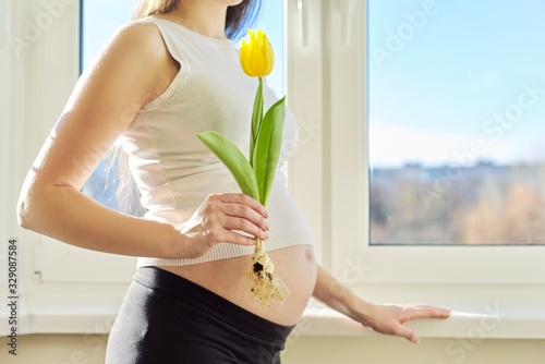 Portrait of pregnant woman with one yellow tulip flower
