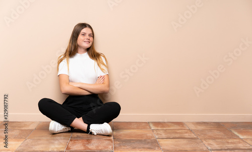 Ukrainian teenager girl sitting on the floor with arms crossed and looking forward