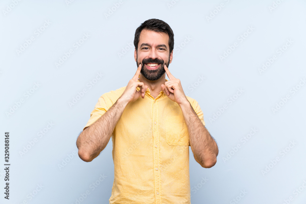 Fototapeta premium Young man with beard over isolated blue background smiling with a happy and pleasant expression