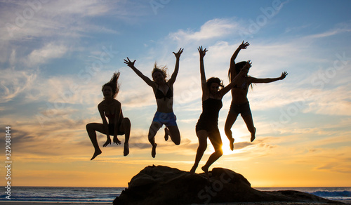 Silhouette of four beautiful women jumping off a rock on a beach at sunset or sunrise.