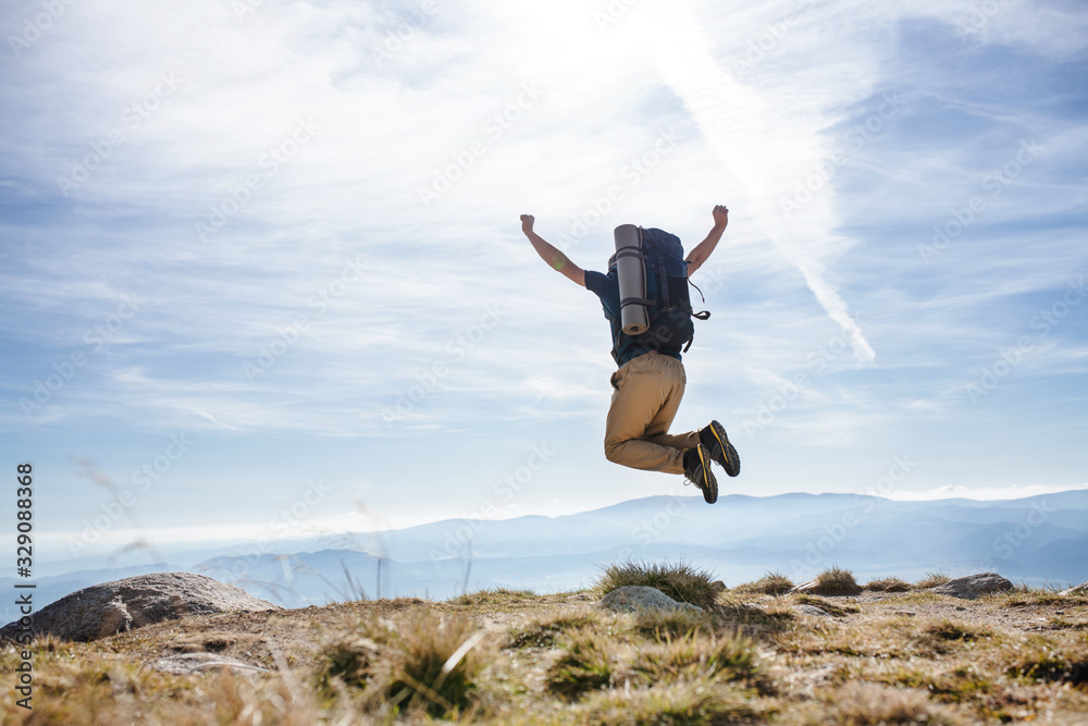 Rear view of man with backpack hiking in mountains in summer, jumping. Rear view of man with backpack hiking in mountains in summer, jumping.