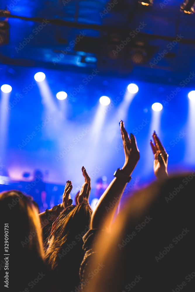 A crowd of people raising their arms up during a concert. They are enjoying the music. Selective focus.