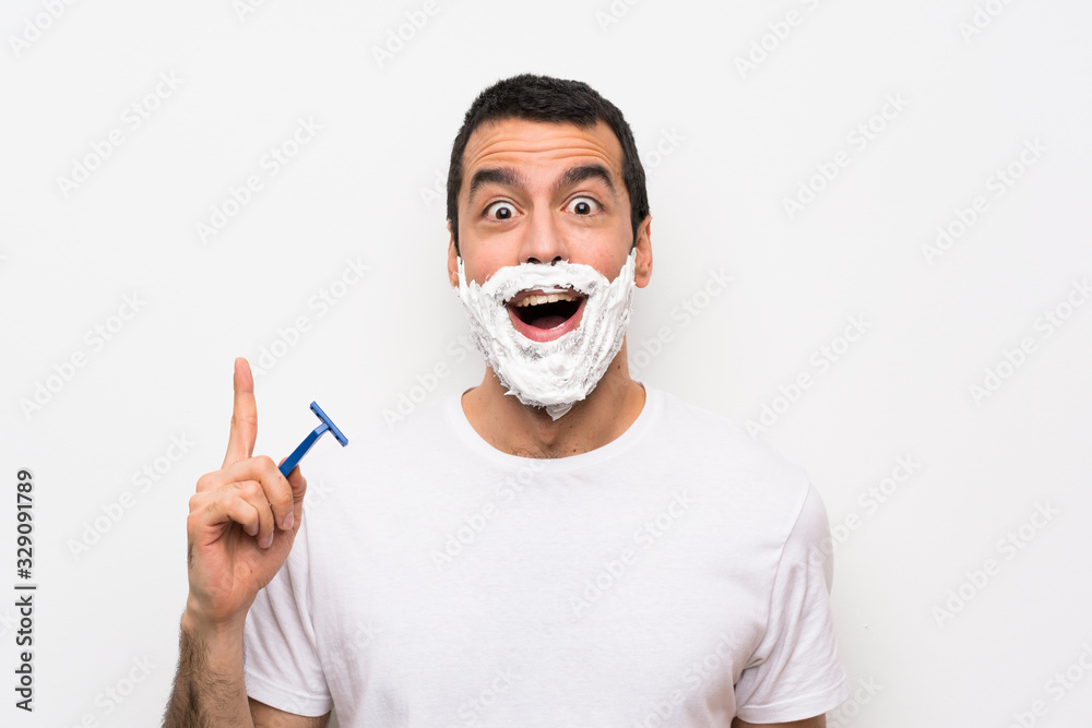 Man shaving his beard over isolated white background thinking an idea pointing the finger up