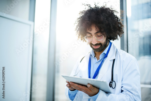 Portrait of male doctor standing in hospital, using tablet.