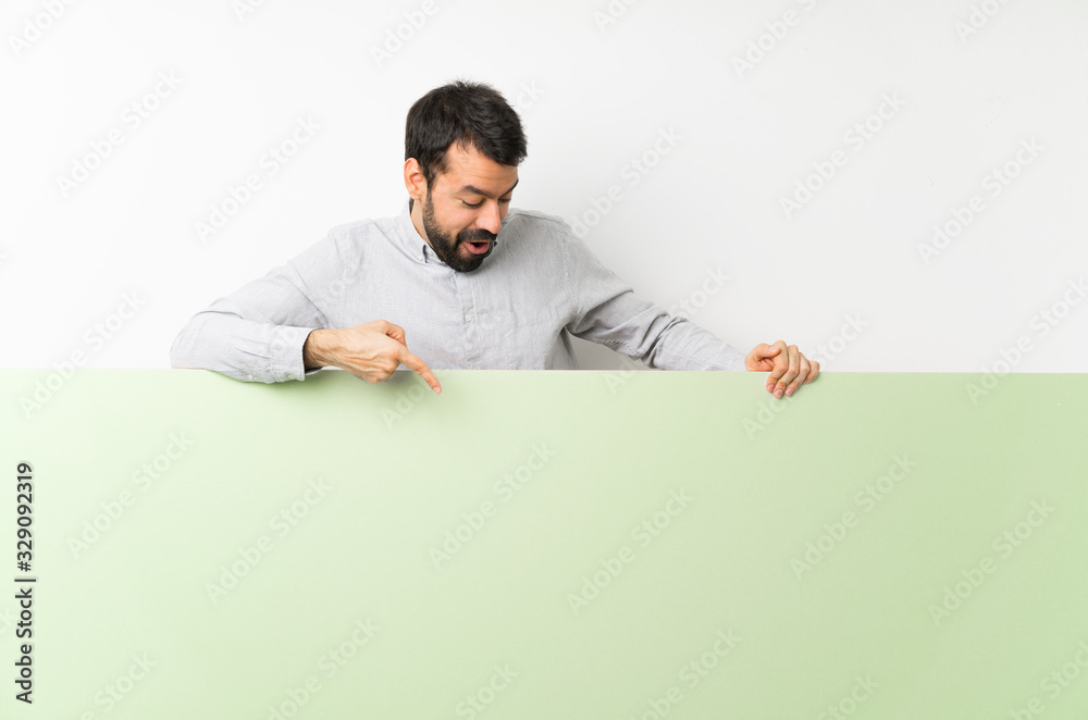Young handsome man with beard holding a big green empty placard and pointing it Young handsome man with beard holding a big green empty placard and pointing it