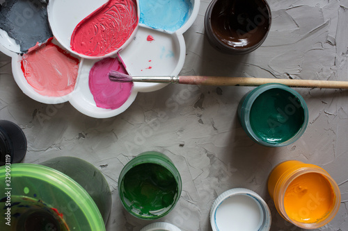 Gouache for drawing different colors with brushes on a gray texture background. Gouache cans are randomly located. Background gray textural brush strokes
