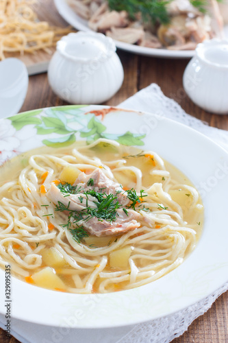 Homemade noodles with chicken in a white plate on a wooden table, selective focus