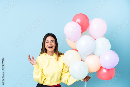 Woman holding balloons in a party over isolated blue background laughing © luismolinero
