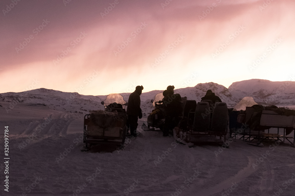 Russia, Murmansk.10.01.2020. a group of researchers in the Arctic tundra, near snowmobiles and a pink sunset above them. On the background of icy hills and a snowstorm. editorial use only.