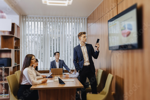 Meeting of office workers at the table, looking at the presentation with diagrams on the TV