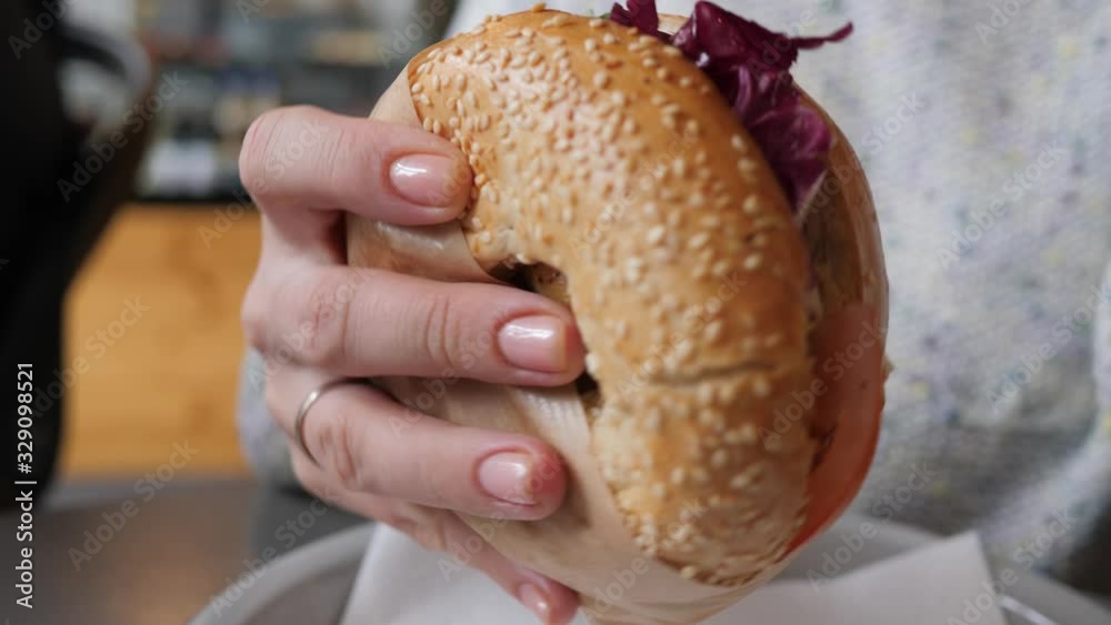 Bagel sandwich closeup woman holds and eat brunch food in the morning sitting in cafe