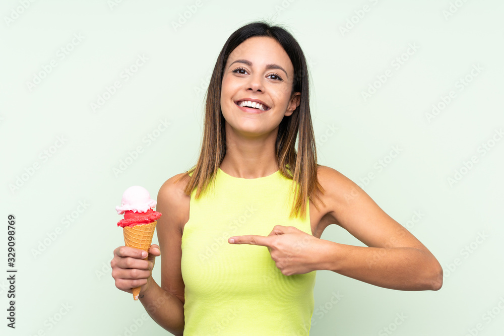Brunette woman holding a cornet ice cream over isolated green background and pointing it Brunette woman holding a cornet ice cream over isolated green background and pointing it
