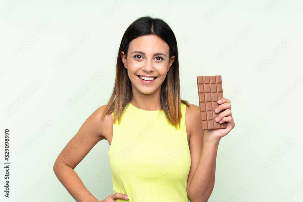 Woman over isolated green background taking a chocolate tablet and happy