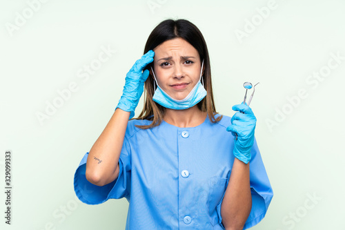 Woman dentist holding tools over isolated green background unhappy and frustrated with something. Negative facial expression