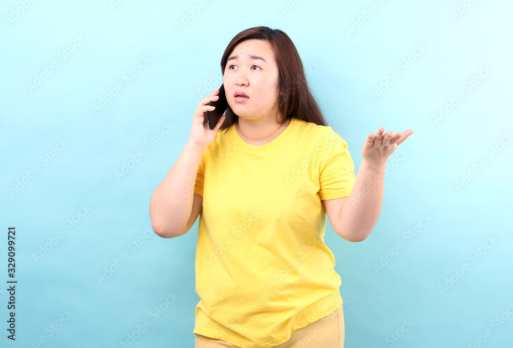 Close up of shocked Asian woman hearing bad news over phone, scared female amazed by negative message received talking on cell, frustrated girl,isolated on blue background in studio.